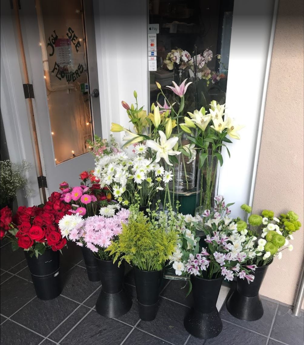 red roses, lilies, and other flowers at the doorway of You See Flowers