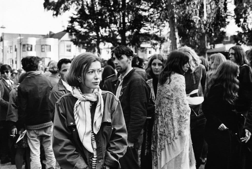 black and white photo of Didion in the 1960s at a gathering in San Francisco's Haight-Ashbury