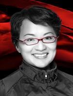 Headshot of Judy Tan, PhD, wearing a black jacket and red glasses, in front of a vibrant red background.